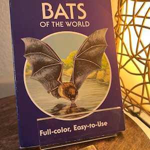 May include: A Golden Guide book titled "BATS OF THE WORLD" with a bat illustration on the cover. The cover is dark blue with white text and a picture of a bat drinking water. The book is labeled "Full-color, Easy-to-Use".