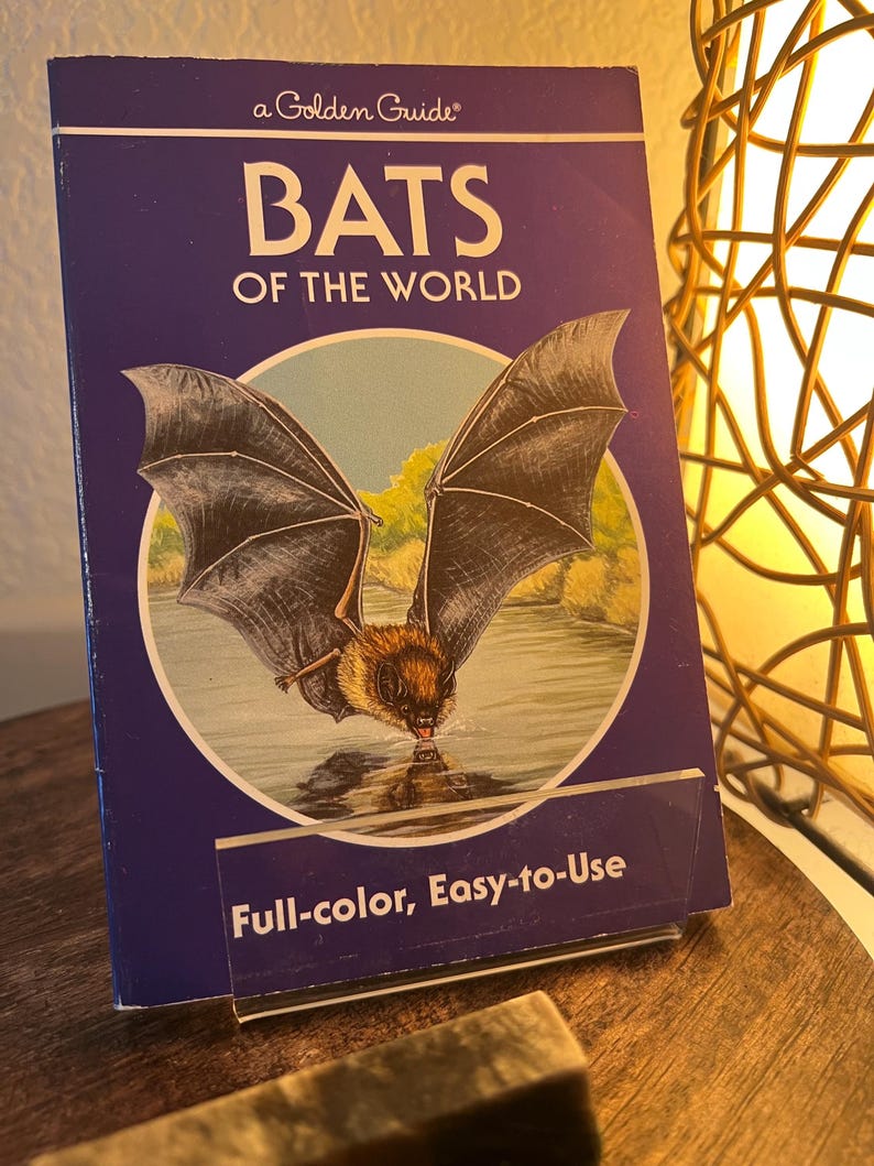 May include: A Golden Guide book titled "BATS OF THE WORLD" with a bat illustration on the cover. The cover is dark blue with white text and a picture of a bat drinking water. The book is labeled "Full-color, Easy-to-Use".