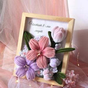 May include: A wooden framed floral arrangement featuring handmade fabric flowers in shades of pink, purple, and white. The arrangement includes a tulip and other flower types, with green leaves. The text "Честит 8-ми март" is visible.