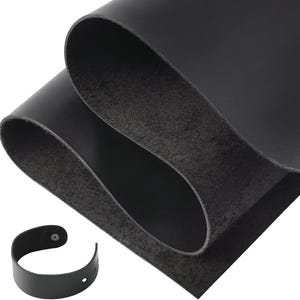 May include: Close-up of black leather sheets, with a curved black leather strap with a button and a hole. The leather sheets are folded over, revealing a textured underside. The strap is likely for a watch or bracelet.