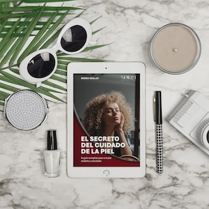 May include: A flat lay featuring a white tablet displaying a book cover with the title "EL SECRETO DEL CUIDADO DE LA PIEL". Other items include white sunglasses, a compact mirror, a candle, a pen, a camera, and a bottle of nail polish.