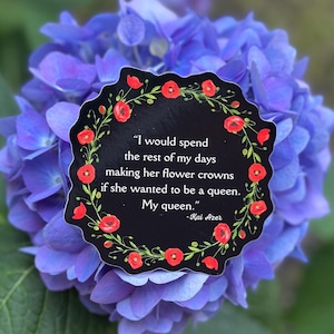 May include: A black sticker with a floral border of red poppies and green leaves, featuring the quote "I would spend the rest of my days making her flower crowns if she wanted to be a queen. My queen." set against a backdrop of blue hydrangea flowers.