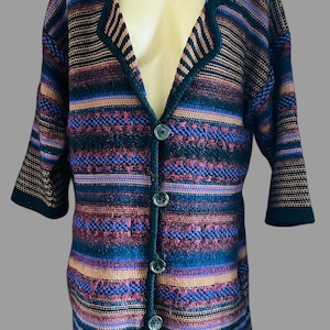Könnte beinhalten: Eine langärmelige Strickjacke mit einem mehrfarbigen horizontalen Streifenmuster in Schwarz, Violett, Blau und Orange. Das Kleidungsstück hat einen Schalkragen, vier dunkle Knöpfe auf der Vorderseite und eine durchgehend strukturierte Strickoptik.