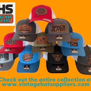 May include: A collection of trucker hats in various colors, featuring embroidered patches with text and graphics. The hats have mesh backs and curved brims. The image includes the text "VHS VINTAGE HAT SUPPLIERS" and "Check out the entire collection at www.vintagehatsuppliers.com."