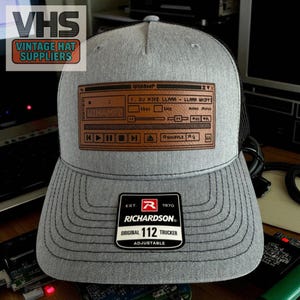 May include: Gray trucker hat with a Winamp graphic on a brown patch. The hat features the text "WINAMP" and "DJ MIKE LLAMA - LLAMA WHIPP". The hat also has a black mesh back and a Richardson patch.