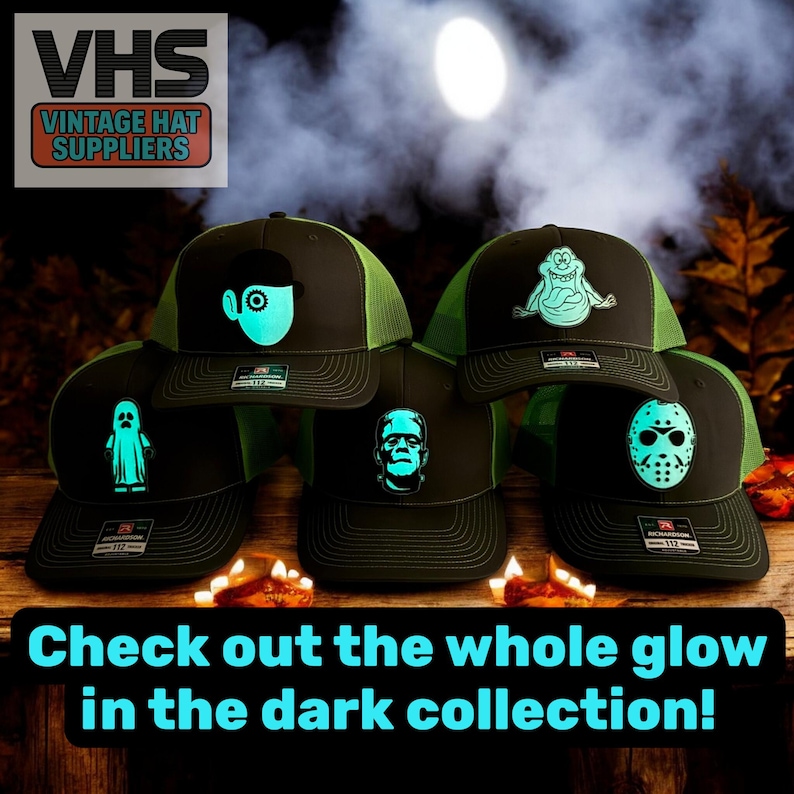 May include: A collection of black trucker hats with neon green mesh and glow-in-the-dark designs. The designs include a ghost, Frankenstein's monster, a monster, and a mask. The hats are displayed on a wooden surface with candles.