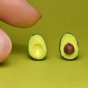 May include: Two miniature avocado halves, one with a seed, on a green background.