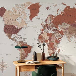 May include: A detailed world map in shades of brown and beige serves as a backdrop for a wooden desk. A green lamp, books, and a vase with flowers are on the desk. A green chair is in front of the desk. The map includes the text "CANADA" and "UNITED STATES".