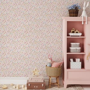 May include: A pink nursery scene with floral wallpaper and a matching cabinet. The cabinet holds toys and decorative items. A woven basket with a doll and pillow sits beside a stack of suitcases. A star-shaped light and wooden blocks complete the scene.