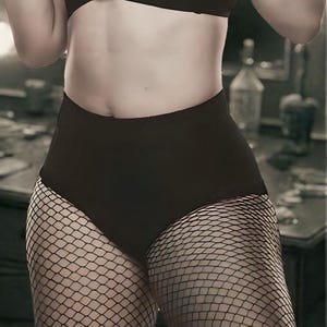 May include: A monochrome image featuring a person in a black bra, high-waisted shorts, and fishnet stockings. The image includes the text "ALL ELITE AEW WRESTLING".