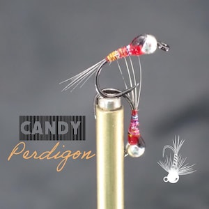 May include: Close-up of a Candy Perdigon fishing fly. The fly features a black hook, red and iridescent body, and a silver bead head. The fly is designed for fly fishing.