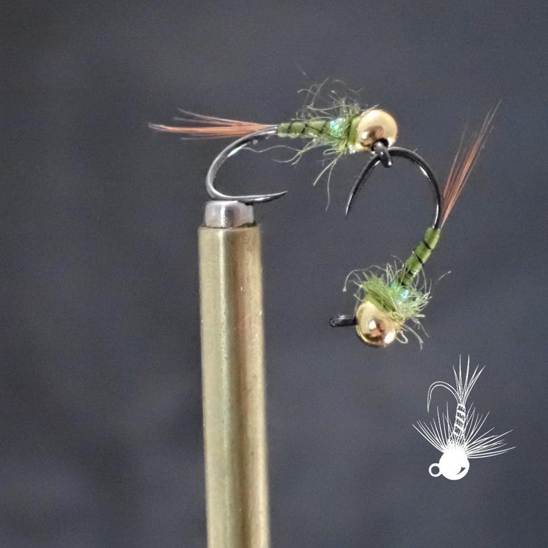 May include: Two handmade fishing flies. Each fly features a gold bead head, a curved hook, and a body of green and brown materials. The flies are designed for fly fishing. One fly is attached to a brass rod.