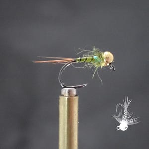 May include: A close-up of a fishing fly with a gold-colored head, green body, and brown and orange tail feathers. The fly is attached to a silver hook and mounted on a gold-colored post. The background is a solid gray.