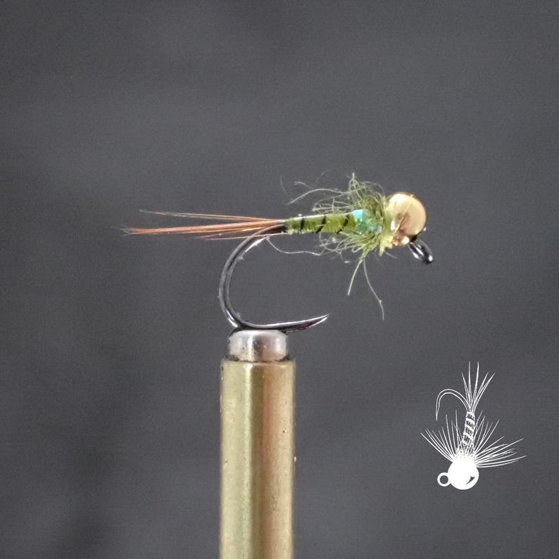 May include: A close-up of a fishing fly with a gold-colored head, green body, and brown and orange tail feathers. The fly is attached to a silver hook and mounted on a gold-colored post. The background is a solid gray.