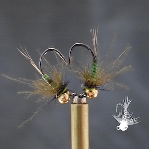 May include: Two handmade fishing flies. Each fly features a curved hook, a gold-colored bead, and a body wrapped in green thread. The flies have brown and tan feather-like materials attached, creating a natural appearance. The flies are designed for angling.