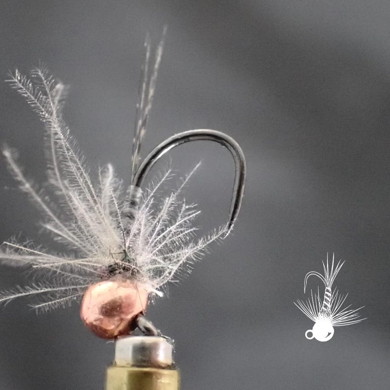 May include: Close-up of a fly fishing lure. The lure features a silver hook, a copper-colored bead, and delicate white feathers. A small, white line drawing of the lure is in the lower right corner against a gray background.