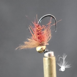May include: A close-up of a handmade fishing fly. The fly has a curved silver hook, a gold-coloured bead, and a body of reddish-brown and tan fibres. The fly is designed for angling.