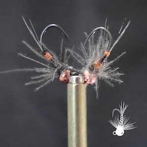May include: Close-up of two handmade fishing flies. Each fly features a curved hook, a copper-colored body, and delicate, feathery wings. The flies are mounted on a gold-colored metal rod, showcasing intricate craftsmanship.