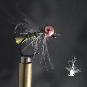 May include: A close-up of a fly fishing lure. The lure features a copper-colored bead head, a dark body, and delicate, feathery wings. The hook is black, and the lure is mounted on a gold-colored post. A white line drawing of a fly is in the lower right corner.