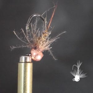May include: A fishing fly lure featuring a metallic copper-colored bead head, a curved steel hook, and a body constructed from textured brown fibers and thin, wispy filaments. A small white line-art illustration of the fly is visible in the corner.