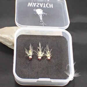 May include: A clear plastic box with the word "WATCH" printed on the lid, containing three fishing flies. The flies have a pink bead head, yellow body, and white feather wings, set against a black foam insert.