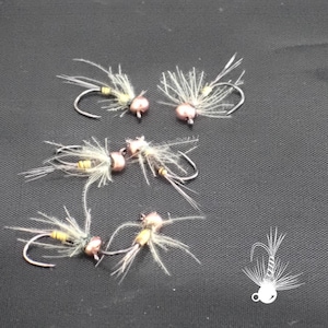 May include: A collection of handmade fishing flies. Each fly features a curved hook, a small, round, copper-colored bead, and delicate, feathery wings. The flies are arranged on a dark surface, showcasing their intricate design and craftsmanship.