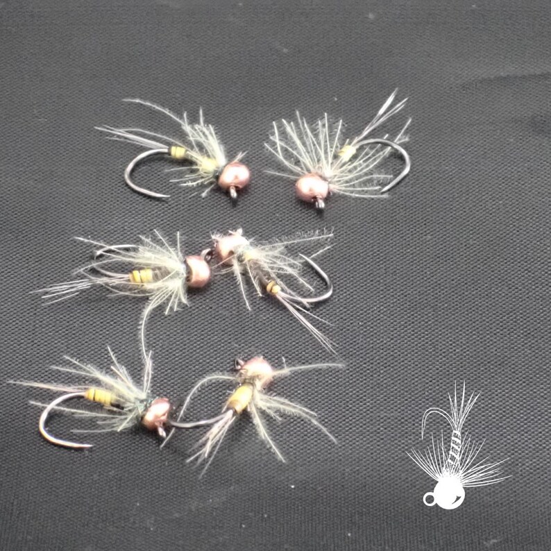 May include: A collection of handmade fishing flies. Each fly features a curved hook, a small, round, copper-colored bead, and delicate, feathery wings. The flies are arranged on a dark surface, showcasing their intricate design and craftsmanship.