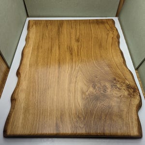 May include: A rectangular wooden chopping board with a natural edge. The board is made of light brown wood with a visible grain pattern. The edges are uneven, giving it a rustic appearance. It is likely used for food preparation.