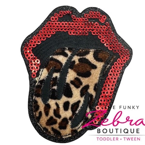 May include: A black, sequined patch in the shape of a mouth with a leopard print tongue. The lips are outlined with red sequins. The patch has the text "Zebra Boutique" and "Toddler • Tween".
