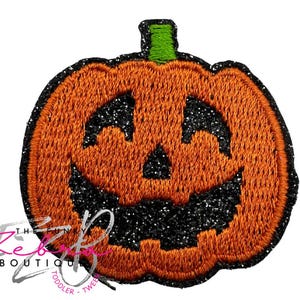 May include: Orange embroidered pumpkin patch with a black glitter face and outline. The pumpkin has a green stem. The Fun Zebra Boutique logo is in the lower left corner.