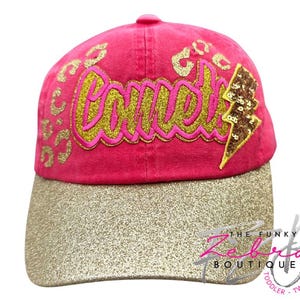 May include: A pink baseball cap with a gold glitter brim. The cap features the word "Comet" in gold script, leopard print accents, and a sequined lightning bolt. The Funky Zebra Boutique logo is visible.