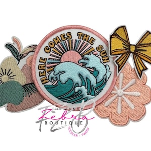 May include: A collection of embroidered patches in various shapes and designs. Includes a round patch with a sun and wave design, a yellow bow, and floral and leaf designs. The round patch reads "HERE COMES THE SUN".