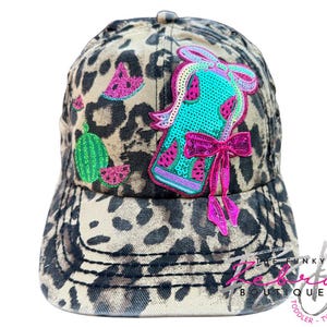 May include: A leopard print baseball cap with watermelon and bow embellishments. The cap features a turquoise and pink sequined watermelon design, with additional watermelon slice patches.