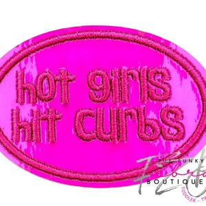 May include: A bright pink embroidered patch with the phrase "hot girls hit curbs" in a bold, stylized font. The patch has a textured appearance and an oval shape. The patch is a fun accessory.