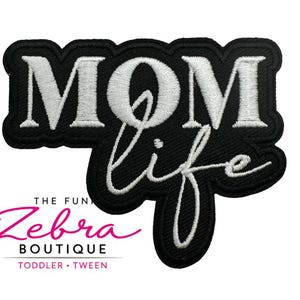 May include: Black embroidered patch with the words "MOM life" in white script. The patch has a black border and includes the text "THE FUN Zebra BOUTIQUE TODDLER • TWEEN" in pink and black.