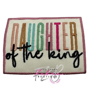May include: Embroidered patch with the words "DAUGHTER of the king" in various colors. The patch has a pink border and a cream-colored background. The text is in black, pink, teal, and brown.