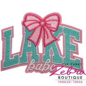 May include: Embroidered patch with the word "LAKE" in teal block letters, topped with a pink bow. The word "babe" is below "LAKE" in cursive. The patch has a pink border and the text "THE FUNKY Zebra BOUTIQUE TODDLER • TWEEN".