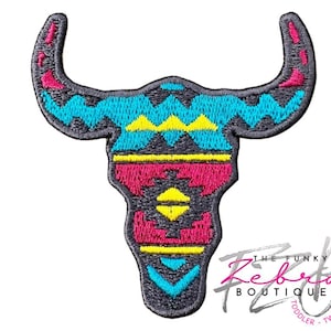 May include: Embroidered patch in the shape of a bull skull with a southwestern design. The patch features a gray outline with turquoise, yellow, and pink geometric patterns. The Funky Zebra Boutique logo is in the bottom right corner.