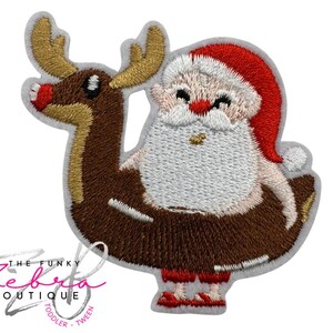 May include: Embroidered patch featuring Santa Claus riding a reindeer-shaped float. Santa wears a red hat and suit with a white beard. The reindeer is brown with gold antlers. The patch has a gray border and the text "THE FUNKY ZEBRA BOUTIQUE TODDLER TWEEN".