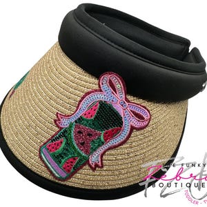 May include: A straw visor with a black brim and a decorative watermelon design. The watermelon design is green, red, and pink, with a sequined outline. The visor is designed for sun protection and has a comfortable fit.