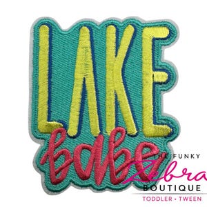 May include: Embroidered patch with the words "LAKE BABE" in yellow and pink, outlined in teal. The patch has a white border and is against a white background. The Funky Bra Boutique logo is in the bottom right corner.