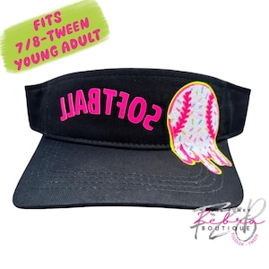 May include: Black visor with the word "SOFTBALL" in bright pink letters. A baseball-shaped patch with pink stitching and colorful sprinkles is on the side. The visor is designed to fit 7/8-Tween Young Adult.