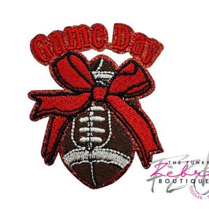 May include: A decorative patch featuring a football design with a red bow and the words "Game Day" in glittery red letters. The football is brown with white stitching. The patch is likely for apparel or accessories.