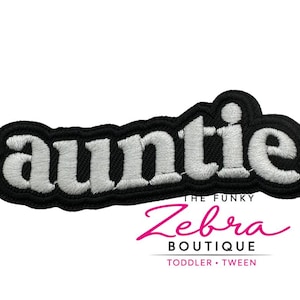 May include: Embroidered patch with the word "auntie" in white, outlined in black. The patch has a black border. Below the patch is the text "THE FUNKY Zebra BOUTIQUE TODDLER • TWEEN" in pink and black.