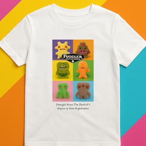 Op de afbeelding: Wit T-shirt met een kleurrijke afbeelding van zes Fuggler-monsters in een raster, met de tekst "Fuggler Funny Ugly Monster" en "Straight From The Dentist's Office of Your Nightmares."