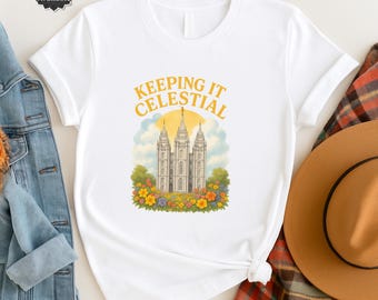 May include: White t-shirt with the text "KEEPING IT CELESTIAL" above a graphic of a white building with three spires, surrounded by colorful flowers. The shirt has short sleeves and a crew neck.