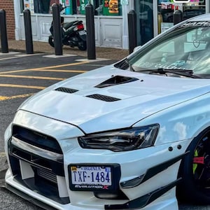 Könnte beinhalten: Eine weiße Mitsubishi Lancer Evolution X Limousine mit belüfteter Motorhaube, schwarzen Frontstoßstangenakzenten und einem Virginia-Nummernschild mit der Aufschrift TXF-1484. Der Text SPEEDMEMORY und EVERY GREAT ACHIEVEMENT BEGINS WITH A DREAM ist eingeblendet.