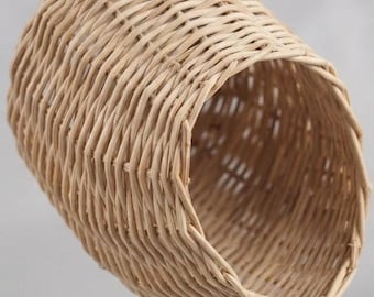May include: A cylindrical hanging basket crafted from light tan woven wicker material. The structure features a hollow interior and a single metal hook attached to the top edge for suspension, showcasing a natural texture and a simple open design.