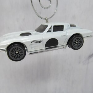 May include: White die-cast toy car ornament with black wheels and a black "Hot Wheels" logo on the side. The car has a black circle on the side.