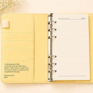 May include: Open yellow leather binder with lined paper and a metal ring binder. The left side has pockets and an inscription: "To My Beautiful Wife...Forever yours, Mike." The right side has a notepad with the word "notes" at the top.